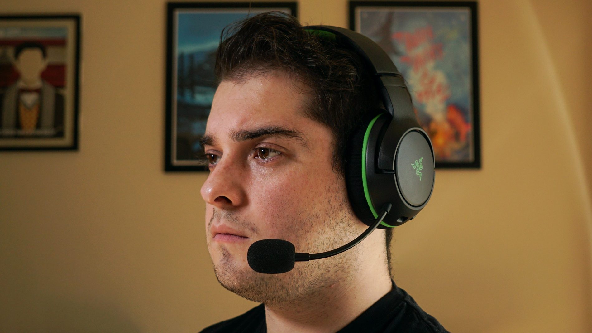 Razer Kaira headshot A man wears the Razer Kaira Wireless sitting at a computer, with posters for My Brother, My Brother and Me, and Canada Heritage Minutes in the background.
