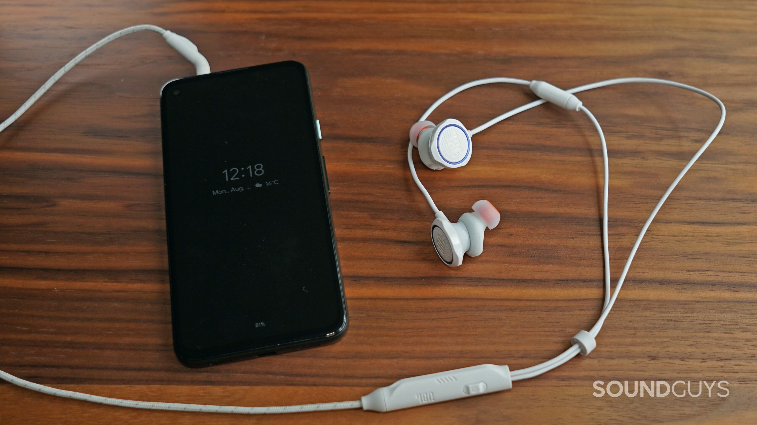 JBL-Quantum-50-Phone-shot The JBL Quantum 50 gaming earbuds lays on a wooden table plugged into a Google Pixel 4a's headphone jack.
