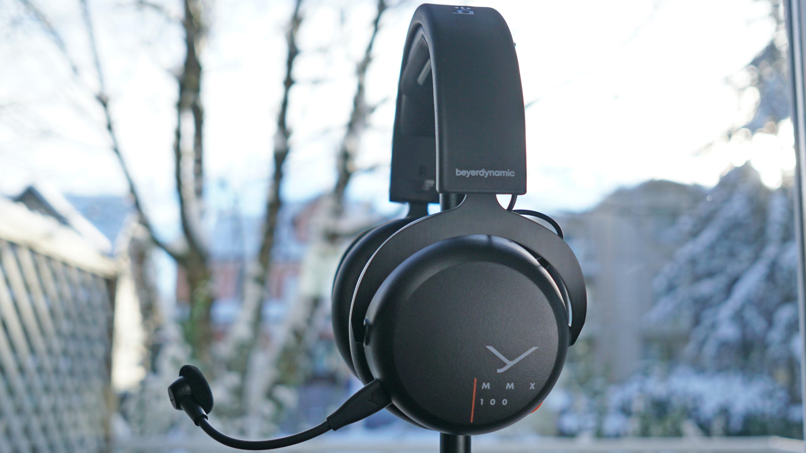 Beyerdynamic-MMX-100-stand-shot The Beyerdynamic MMX 100 gaming headset sits on a headphone stand in front of a window.