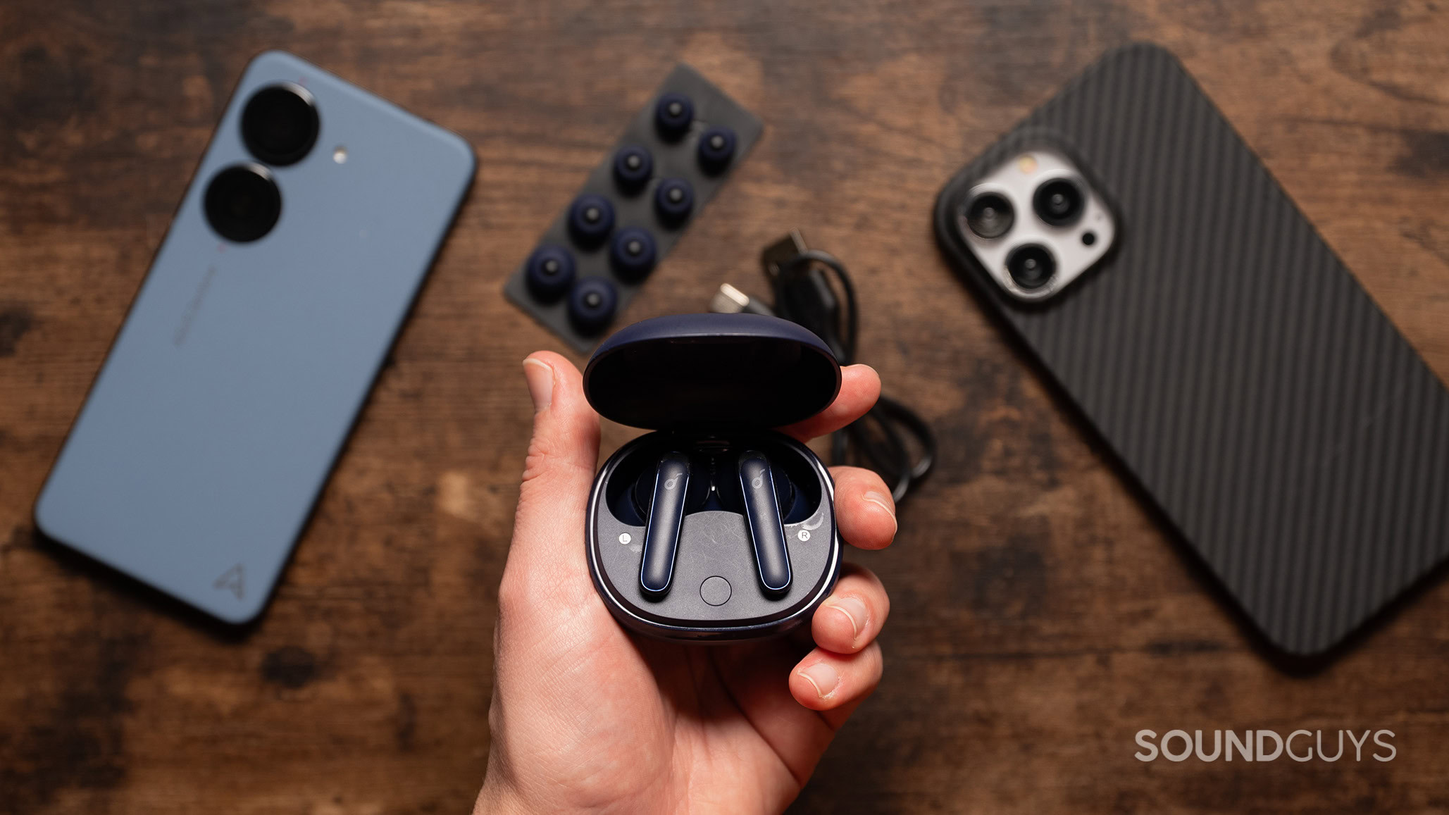 Anker Soundcore Life P3 hero A hand holds the Anker Soundcore Life P3 over a table with two smartphones on it.