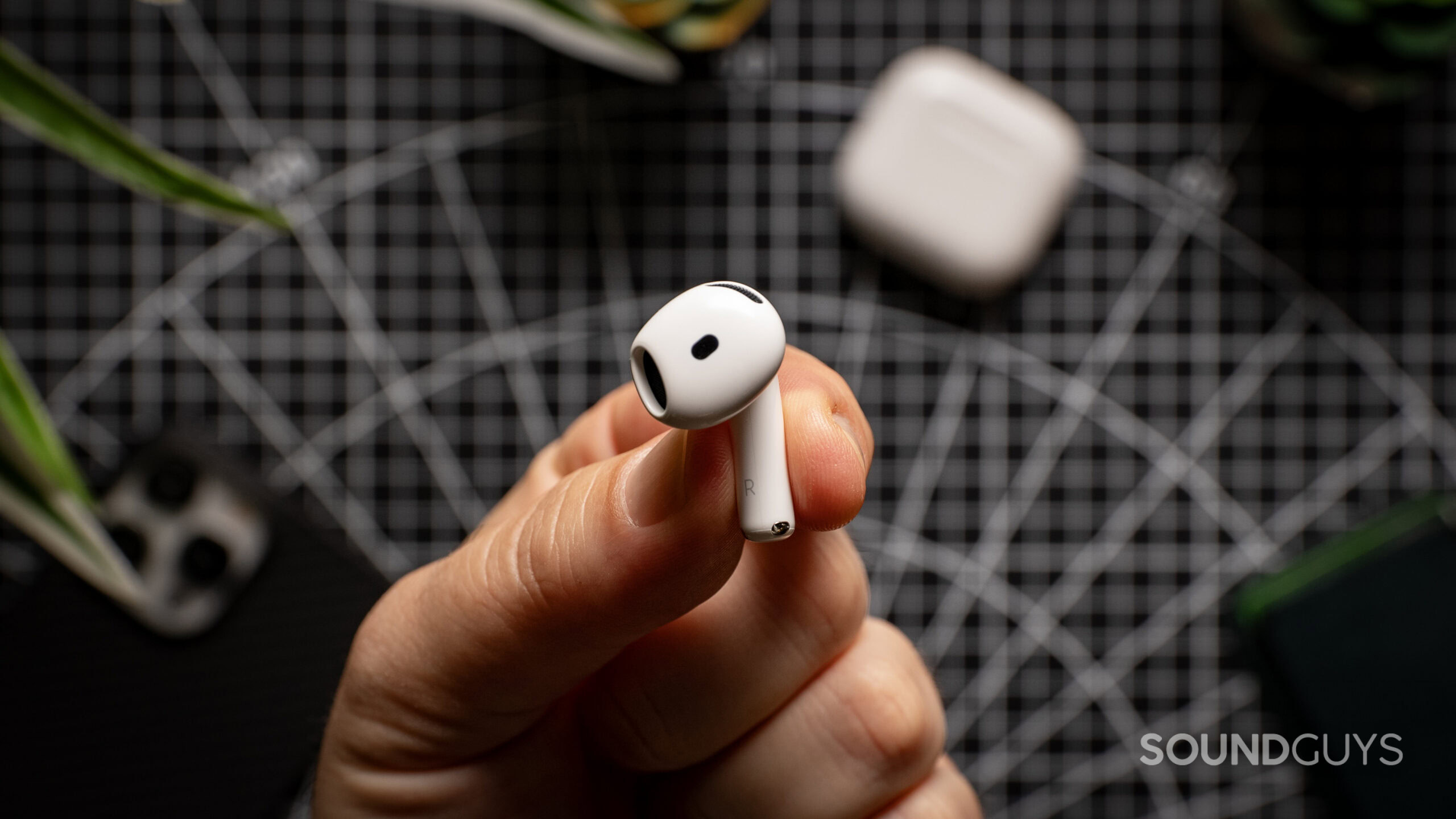 Apple AirPods 4 right earbud in hand side view A hand holds the AirPods 4 earbud over a table.